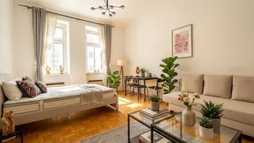 Helles Wohn- und Schlafzimmer mit Parkettboden, großen Fenstern und moderner Einrichtung.