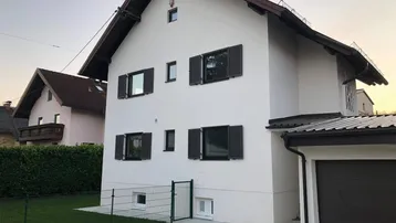 Weiß verputztes Einfamilienhaus mit dunklen Fensterläden und angrenzender Garage.