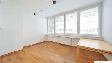 Helles Zimmer mit Parkettboden, großen Fenstern und einem Heizkörper unter der Fensterbank.