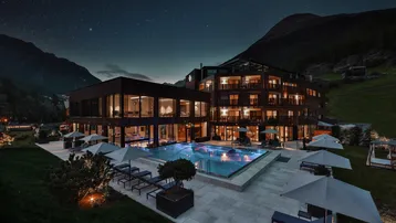 Beeindruckendes modernes Gebäude mit beleuchtetem Außenpool und Bergblick bei Nacht unter klarem Sternenhimmel.
