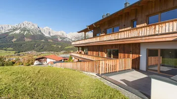 Modernes Holzgebäude mit mehreren Balkonen und Terrassen in einer malerischen Berglandschaft.