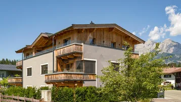 Modernes Gebäude mit Holzfassade, Balkonen und Bergblick unter blauem Himmel.