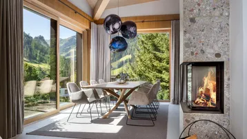 Heller Essbereich mit Holzbalkendecke, Kamin und Panoramafenstern mit Bergblick.