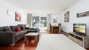 Heller Wohn- und Essbereich mit bequemer Couch, Fernseher und Zugang zur Terrasse mit Gartenblick.