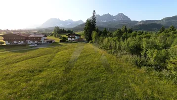 Weitläufige grüne Landschaft mit traditionellen Häusern und majestätischem Bergblick im Hintergrund.