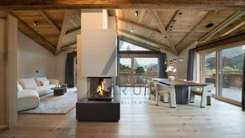 Geräumiger Wohn-Essbereich mit modernem Kamin, Holzbalkendecke und weitem Bergblick.