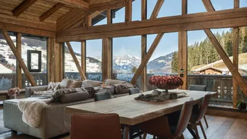 Helles Wohn- und Esszimmer mit Holzbalken, großen Fenstern und Bergblick.