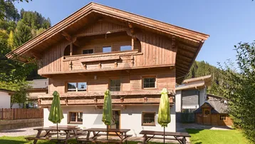 Traditionelles Holzhaus im Chalet-Stil mit Gartenbereich und Picknicktischen unter Sonnenschirmen.