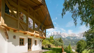 Charmantes Holzhaus mit traditioneller Architektur und atemberaubendem Bergblick unter blauem Himmel.