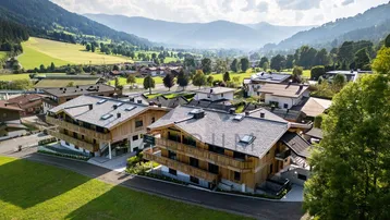 Luftaufnahme einer modernen Wohnanlage mit Holzhäusern in einer malerischen grünen Talandschaft.