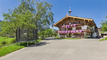 Traditionelles Alpenhaus mit Holzbalkonen, Blumenkästen und Trampolin im Gartenbereich.
