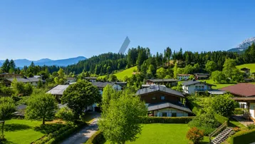 Panoramablick über eine ländliche Siedlung mit grünen Hügeln und bewaldeten Bergen im Hintergrund.
