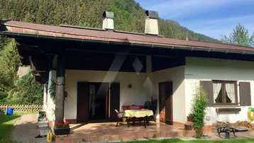 Gemütliche überdachte Terrasse mit Sitzgelegenheiten, umgeben von einem gepflegten Garten und Bergblick.