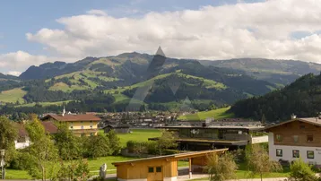 Panoramablick auf die umliegende Berglandschaft und ein Dorf mit grünen Wiesen unter blauem Himmel.