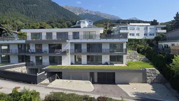 Modernes Mehrfamilienhaus mit Flachdach und großen Fensterfronten in alpiner Umgebung mit Bergblick.