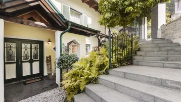 Traditionelles Haus mit Steintreppe und grüner Bepflanzung am Eingangsbereich.