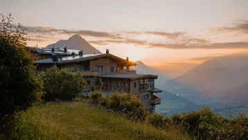 Gebäude auf einem Berghang bei Sonnenuntergang mit atemberaubendem Blick auf die umliegende Berglandschaft.