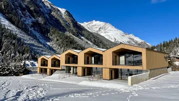 Moderne Gebäude mit Holzfassaden und großen Fenstern in verschneiter Berglandschaft.