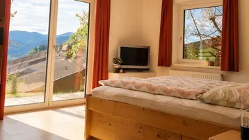 Schlafzimmer mit Holzbett, großen Fenstern und einem atemberaubenden Blick auf die umliegende Berglandschaft.