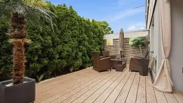 Geräumige Holzterrasse mit Outdoor-Sitzbereich und hohen Hecken für Privatsphäre im Freien.