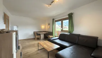 Gemütlicher Wohn-Essbereich mit Ledersofa, Holztisch und Blick ins Grüne.