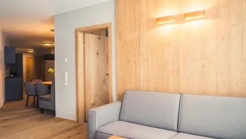 Modernes Wohnzimmer mit Holzwandverkleidung, bequemer Couch und Blick in den Essbereich.