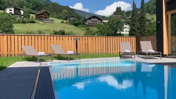 Außenpool mit Liegestühlen und herrlichem Blick auf die grüne Berglandschaft.