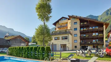 Außenansicht des Gebäudes mit einem erfrischenden Poolbereich, umgeben von grünen Bergen und Rasenflächen.