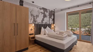 Gemütliches Schlafzimmer mit Holzboden, Hirschmotiv-Wanddekoration und Zugang zum Balkon mit Bergblick.