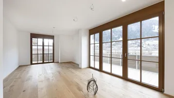 Heller Wohnraum mit Eichenparkett, großen Fenstern und Zugang zum Balkon mit Bergblick.