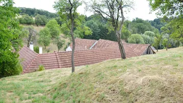 Hügelige Landschaft mit Bäumen und Dächern von Häusern in der Ferne unter bewölktem Himmel.