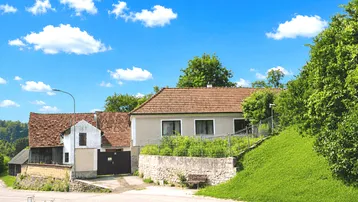 Hausansicht mit Garten und ländlicher Umgebung unter blauem Himmel.