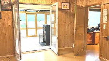Wohnbereich mit Holzvertäfelung und Zugang zu einem hellen Wintergarten mit Kaminofen.
