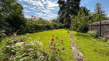 Grüner Gartenbereich mit Rasenfläche, Blumenbeeten und einem Steinpfad unter blauem Himmel.
