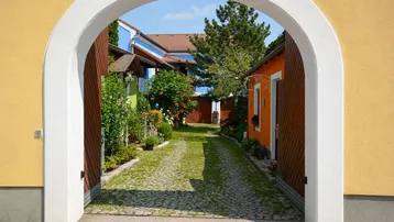 Blick durch einen Torbogen auf einen gepflasterten Innenhof mit bunten Gebäuden und viel Grün.