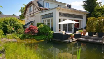Großzügiger Gartenbereich mit Teich, Holzdeck und gemütlicher Sitzecke vor dem Haus.