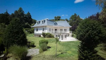 Elegante weiße Villa mit blauem Dach und weitläufigem Garten unter klarem Himmel.