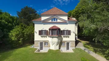Elegante Villa mit historischer Architektur und gepflegtem Vorgarten, umgeben von üppigem Grün.