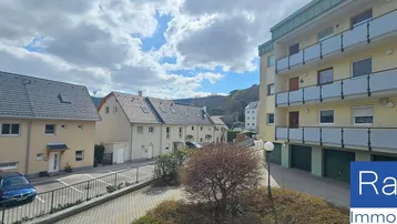 Blick auf eine Wohnsiedlung mit Mehrfamilienhaus, Reihenhäusern und Parkplätzen unter bewölktem Himmel.