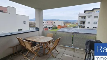 Geräumiger Balkon mit Holztisch und Stühlen, ideal für entspannte Stunden im Freien mit Blick auf die Umgebung.