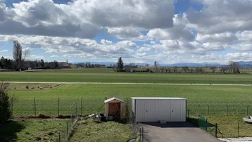 Weitläufiger Blick vom Balkon über grüne Felder und die malerische Landschaft mit Bergen im Hintergrund.