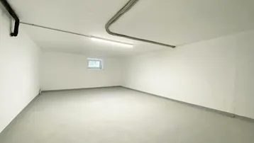 Geräumiger Kellerraum mit weiß gestrichenen Wänden, Betonboden und einem kleinen Fenster.