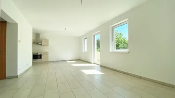 Heller, offener Wohnbereich mit integrierter Küchenzeile, Fliesenboden und Zugang zum Balkon.