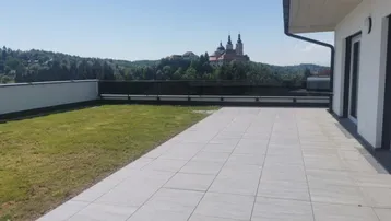 Große geflieste Terrasse mit Rasenfläche und weitem Blick auf ein historisches Gebäude.