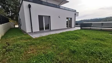 Modernes Gebäude mit weißer Fassade, Terrasse und Rasenfläche im Gartenbereich.