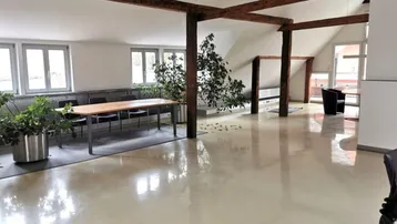 Großer, heller Büroraum im Dachgeschoss mit sichtbaren Holzbalken, glänzendem Boden und viel Tageslicht.