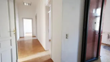 Langer Flur mit Holzboden und mehreren Türen, der zu verschiedenen Räumen führt.