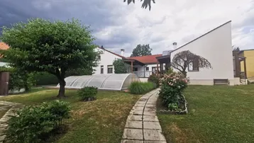 Großer Garten mit gepflegtem Rasen, Bäumen und einem überdachten Poolbereich unter bewölktem Himmel.