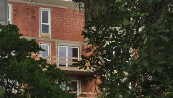 Neubau in Rohbauweise mit sichtbaren Ziegelwänden und provisorischen Balkongeländern, umgeben von Bäumen.