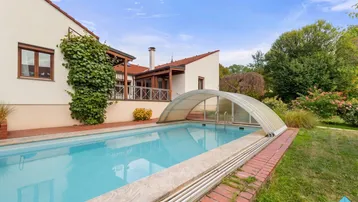 Außenansicht des Hauses mit einem überdachten Swimmingpool und gepflegtem Gartenbereich.